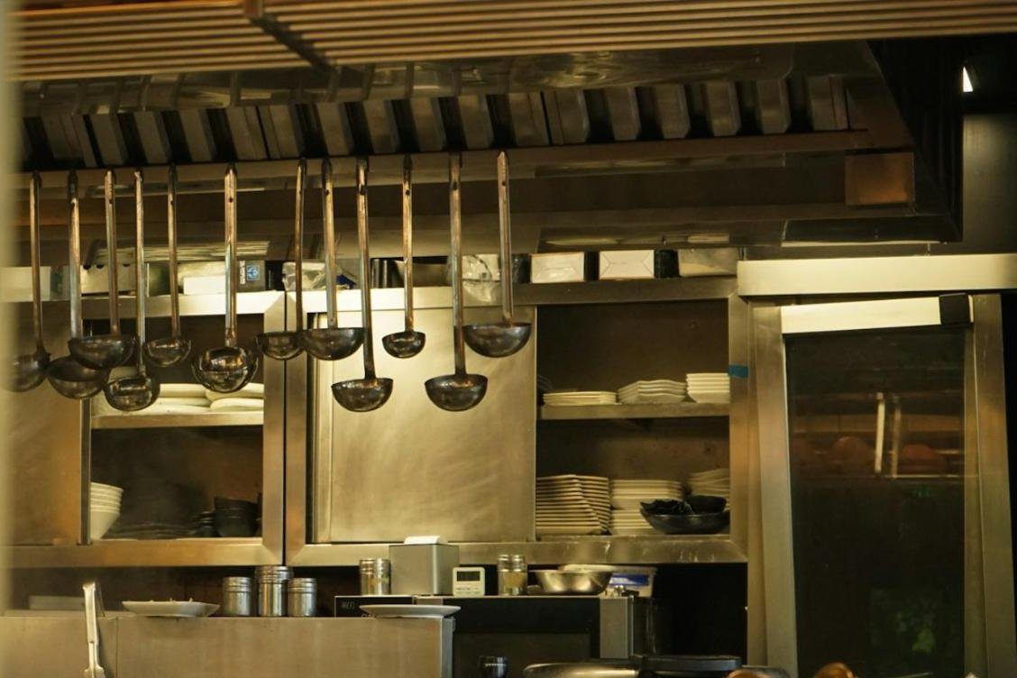 Professional kitchen pass with ladles hanging over a stainless steel shelf
